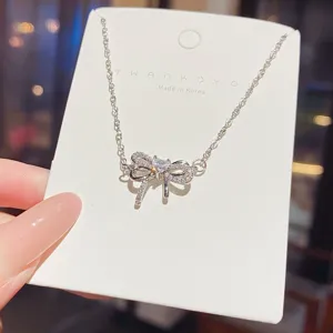 Close-up of a silver-tone bow pendant with clear stones on a fine chain, displayed on a card