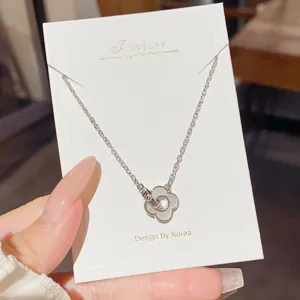 Silver-tone floral pendant with a white enamel-like center, shown on a jewelry card held by hand