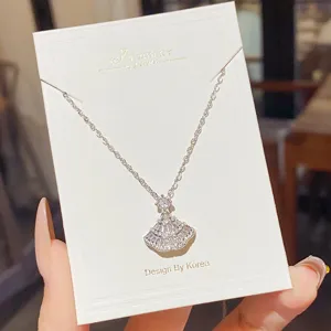 Close-up of a silver-tone necklace with a sparkling fan-shaped pendant displayed on a white card