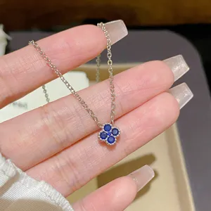 Close-up of a silver-tone chain and four-leaf clover pendant with blue stones, held in hand