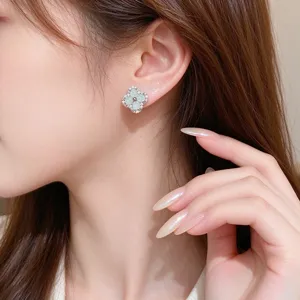 Close-up of a pale green four-leaf clover stud with sparkling stones, shown worn on the ear