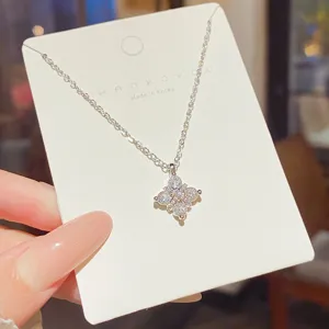 Close-up of a silver-toned fine chain with a sparkling four-petal pendant set with clear stones