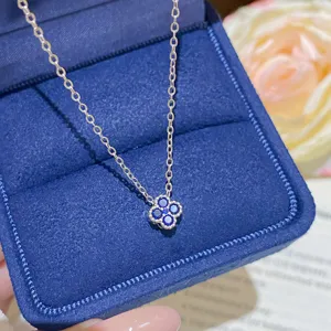 Close-up of blue stones set in a four-petal pendant on a fine chain, resting on navy velvet