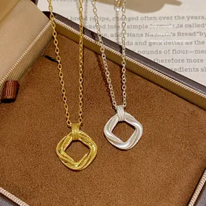 Detail of gold and silver chains with twisted square pendants arranged in a brown jewelry box