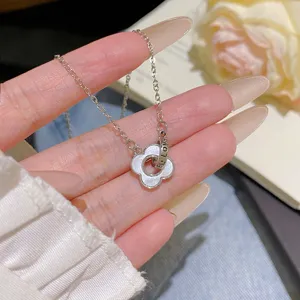 Close-up of a silver chain and four-leaf flower pendant with a pale inlay, held in hand