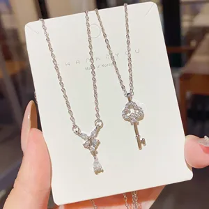Two silver necklaces with sparkling bow and clover-key pendants displayed on a white card
