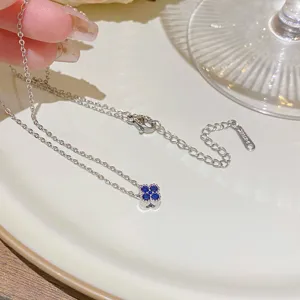 Close-up of a silver-tone necklace chain with a blue four-leaf clover pendant, extender and clasp