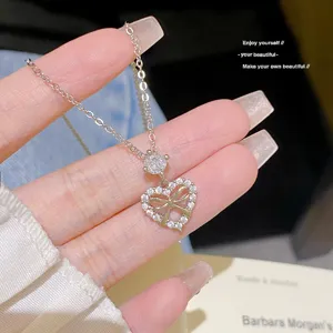 Close-up of a silver-tone heart and bow pendant with clear stones, displayed in a hand