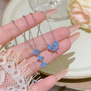 Close-up of silver chains with blue crystal flower pendants displayed across a hand