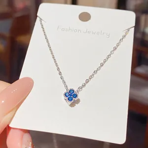 Close-up of a blue flower pendant with sparkling stones on a silver-tone chain, displayed on a card