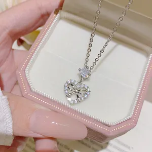 Close-up of a silver-tone chain with a heart-shaped bow pendant, clear stones and an oval accent