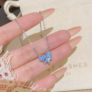 Close-up of a silver-tone chain with a blue crystal flower pendant draped across a hand