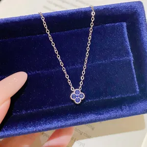 Close-up of a silver-tone chain with a blue four-leaf clover pendant on a velvet box