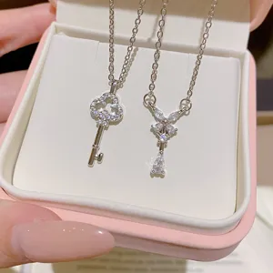 Two silver necklaces with sparkling key and bow pendants, displayed in a white jewelry box