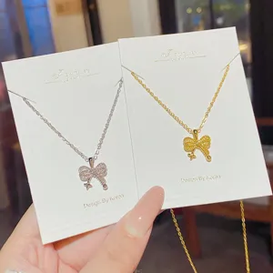 Two delicate bow pendant necklaces in silver and gold, displayed on white jewelry cards