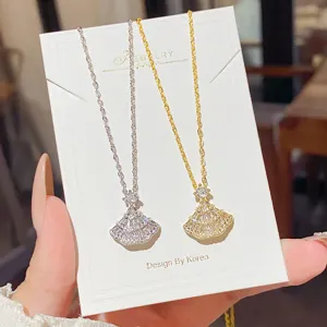 Silver and gold fan-shaped pendants with sparkling stones displayed on a white jewelry card