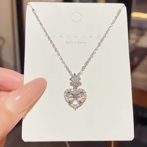 Heart-shaped bow pendant with clear stones and a round accent, displayed on a jewelry card