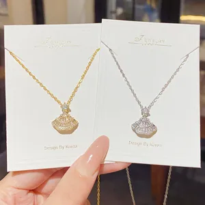 Gold and silver fan-shaped pendants with sparkling stones displayed on white jewelry cards