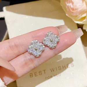 Close-up of sparkling four-leaf clover stud earrings with clear stones, held in a hand