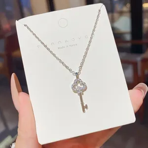 Close-up of a silver key pendant with a sparkling clover-shaped top, displayed on a jewelry card