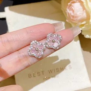 Close-up of pink four-leaf clover stud earrings with clear stones, held in a hand