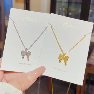 Silver and gold bow pendants with fine openwork detail, displayed on white jewelry cards