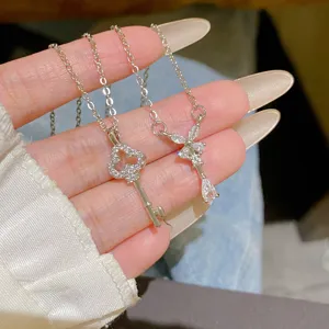 Close-up of two silver-tone key necklaces with bow-shaped crystal pendants held in a hand