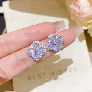 Close-up of purple four-leaf flower stud earrings with sparkling clear stones, held in a hand