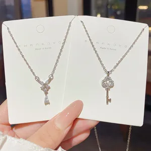 Close-up of two silver-tone necklaces with clear-stone bow and four-leaf clover key pendants