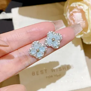 Close-up of blue floral stud earrings with pale blue stones, clear accents, and gold-tone centers