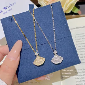 Gold and silver fan-shaped pendants with clear stones on fine chains, shown on blue velvet.