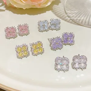 Colorful flower stud earrings with sparkling zirconia stones arranged on a white ceramic dish