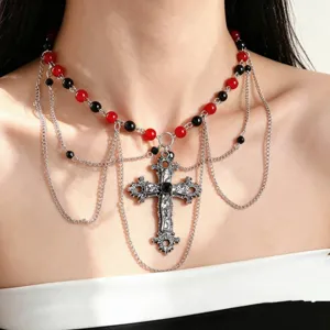 Dettaglio di perline rosse e nere, catene argentate sovrapposte e croce decorata con pietre scure