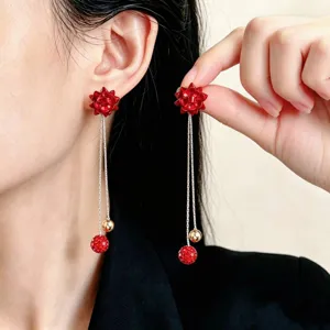Orecchini a fiore rosso con catene argentate e pendenti rossi, indossati e tenuti vicino al viso