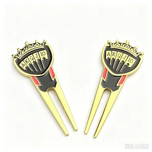 Close-up of two gold-tone golf divot tools with crown-shaped tops and black, red card details