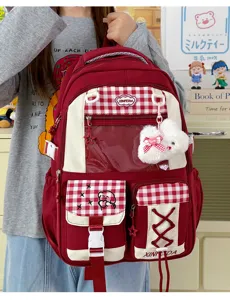 Front view of a red backpack with plaid pockets, clear display pouch and plush bear charm