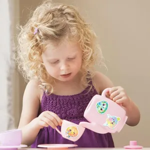 A child uses colorful holographic cartoon stickers to decorate a pink toy teapot and cups