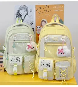 Two pastel backpacks side by side, showing clear front windows, zip pockets and fluffy charms