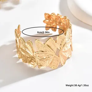 Dettaglio dei motivi a farfalla e foglia in rilievo su un ampio bracciale dorato, con misura