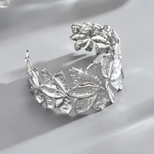 Primo piano di un bracciale rigido aperto argentato, con petali sagomati e dalla texture incisa