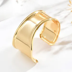 Bracciale rigido aperto dorato, con ampia superficie a specchio e bordi curvi su marmo bianco
