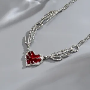 Dettaglio di un cuore smaltato rosso con bordo argentato, unito a una catena scultorea lavorata