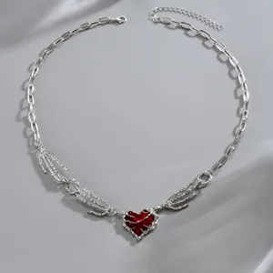 Dettaglio della catena color argento con ciondolo a cuore rosso e motivo di mano scheletrica
