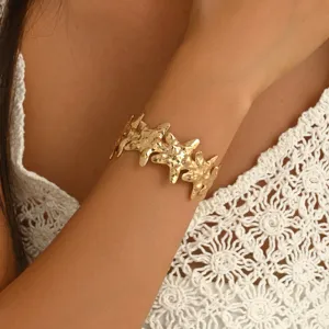 Primo piano di un bracciale dorato martellato a stelle marine indossato al polso con maglia bianca