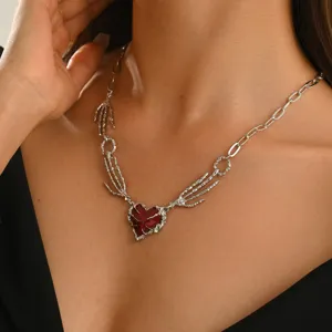 Primo piano del ciondolo a forma di mano scheletrica argentata con cuore rosso scuro sul collo