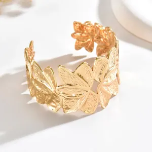 Bracciale rigido aperto dorato, largo e texturizzato, con foglie sovrapposte su fondo bianco