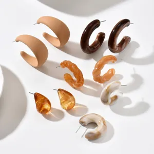 Set di grandi orecchini a cerchio C in resina, beige, marrone e ambra, disposti su fondo bianco