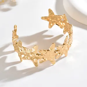 Bracciale rigido aperto dorato con texture martellata e stelle scolpite, su fondo bianco pulito