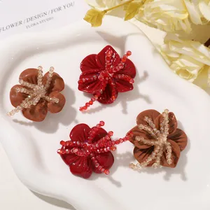 Four red and brown resin flower ornaments with sparkling bead centers, arranged on a white tray