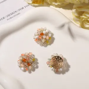 Overhead view of three round beaded floral embellishments in pearl white, peach and clear tones